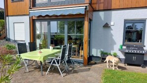 Un patio con mesa y sillas, una parrilla y un perro.