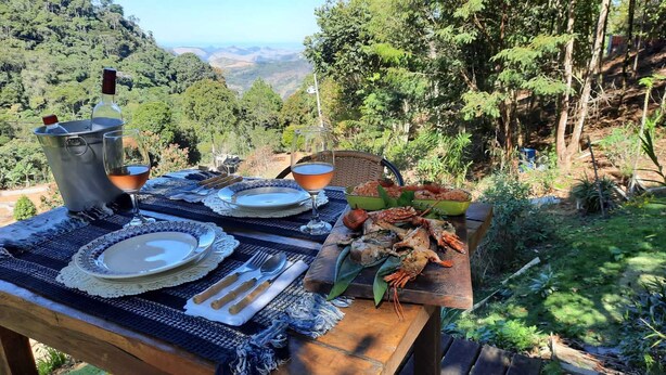 An outdoor dining setup with a scenic view, a metal pot, plates, cutlery, and a bowl of seafood. - Pousada Portaldo Céu  (Domingos Martins)