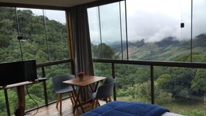 A bedroom with a large window, a bed, a TV, and a small table with chairs. - Pousada Portaldo Céu  (Domingos Martins)
