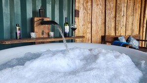 A hot tub with water flowing into it, a wooden shelf with bottles and glasses, and a wooden chair with a blue cushion. - Pousada Portaldo Céu  (Domingos Martins)