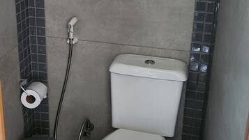 Um banheiro pequeno com vaso sanitário, chuveiro e rolo de papel higiênico.