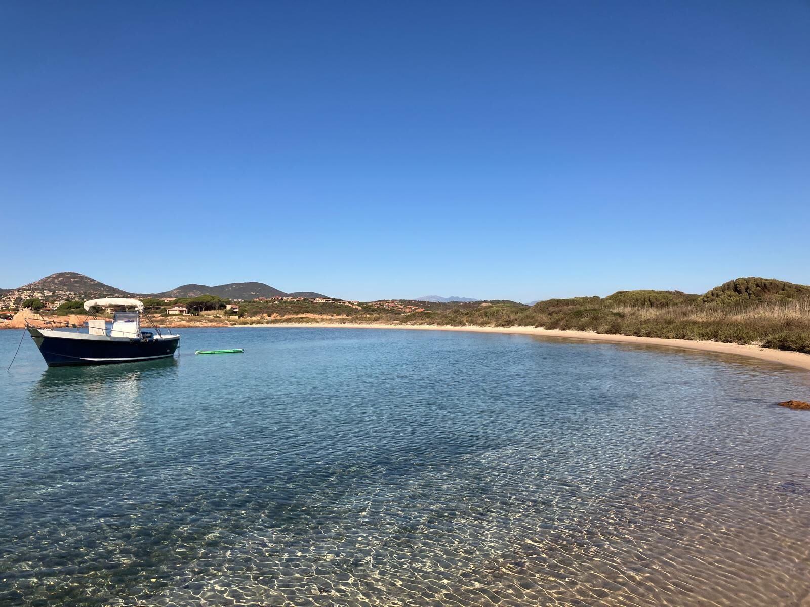 Un bateau sur une eau calme, sous un ciel dégagé, avec des collines qui se dessinent à l’horizon.