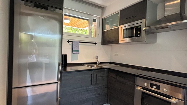 A modern kitchen with stainless steel appliances, a window with a view, and a built-in microwave. - Ulia Apartments- Parking AND Terrace (Donostia)