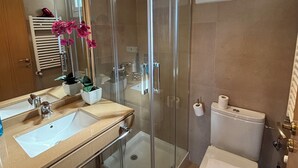 A modern bathroom with a glass-enclosed shower, a double sink vanity, a toilet, and a window. - Ulia Apartments- Parking AND Terrace (Donostia)