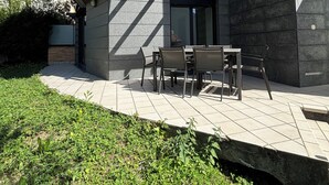 An outdoor patio with a table and chairs, surrounded by a stone wall and a grassy area. - Ulia Apartments- Parking AND Terrace (Donostia)