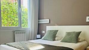 A bedroom with a bed, a radiator, a window with curtains, and a view of greenery outside. - Ulia Apartments- Parking AND Terrace (Donostia)