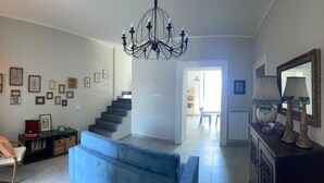 Una sala de estar con una escalera, un sofá azul, una silla de madera, una araña y un comedor al fondo.