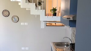 Una cocina moderna con estufa integrada, un lavamanos y una escalera con barandilla. Hay dos plantas en macetas en la escalera.