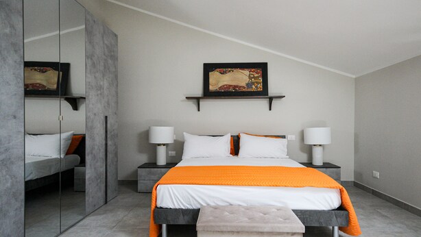Una habitación de hotel moderna con una cama grande, mesitas de noche con lámparas, un espejo y un cuadro en la pared.