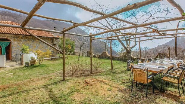 A covered outdoor dining area with a rustic wooden pergola, a stone building with a tiled roof, and a mountainous backdrop. - Villa Maddalena - Scala (Scala)
