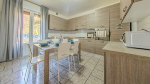 A modern kitchen with wooden cabinets, a dining table set for four, and a microwave on the counter. - Villa Maddalena - Scala (Scala)