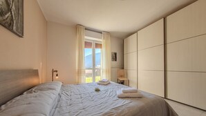 A bedroom with a large bed, a chair, a nightstand, and a view of the outdoors through a window. - Villa Maddalena - Scala (Scala)