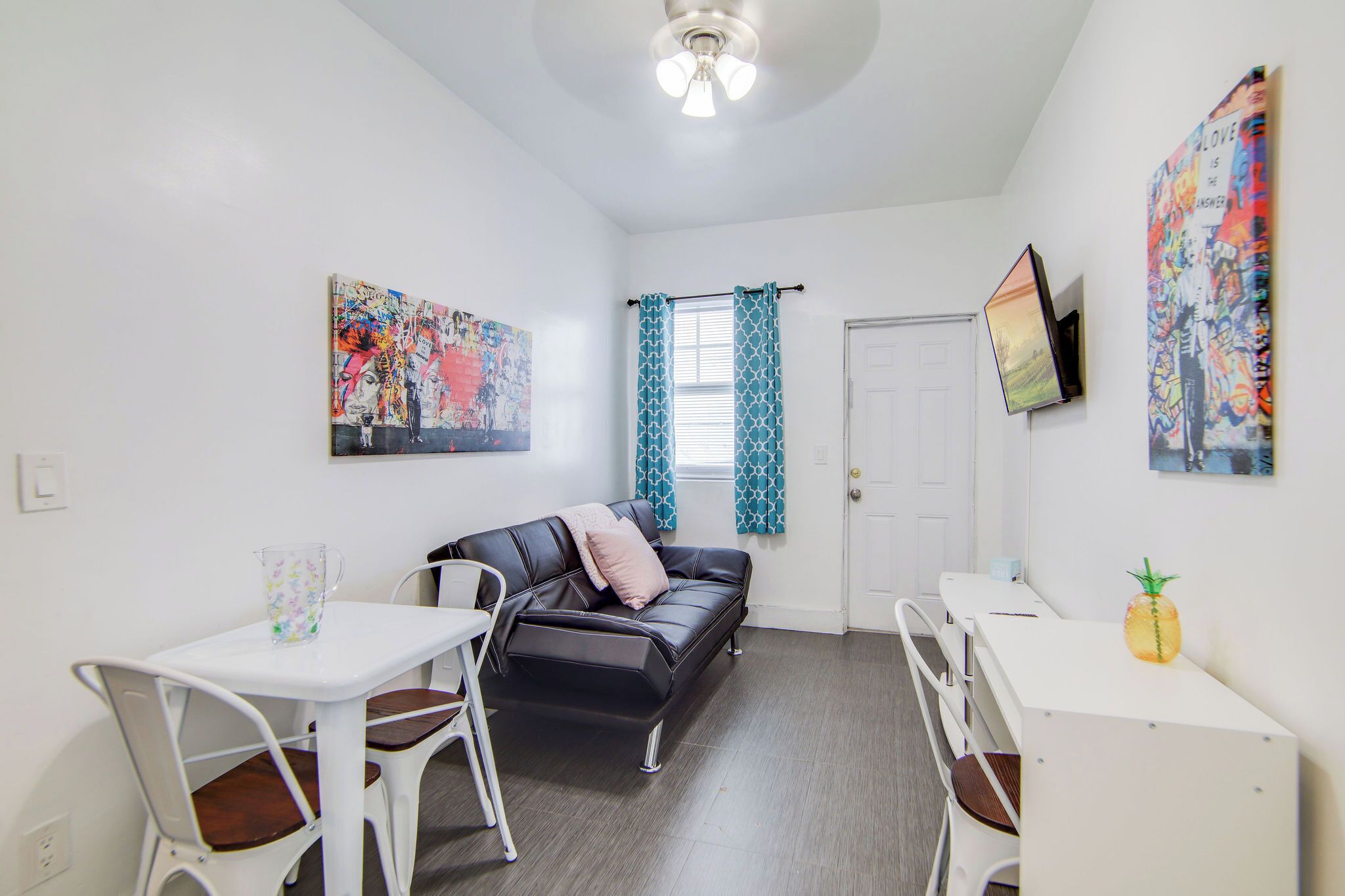 A compact living space with a black leather sofa, white chairs, a small table, and a TV mounted on the wall.