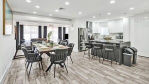 Eine moderne Küche mit weißen Schränken, einer zentralen Kochinsel mit Barhocker und einem Essbereich mit Holztisch und Stühlen.