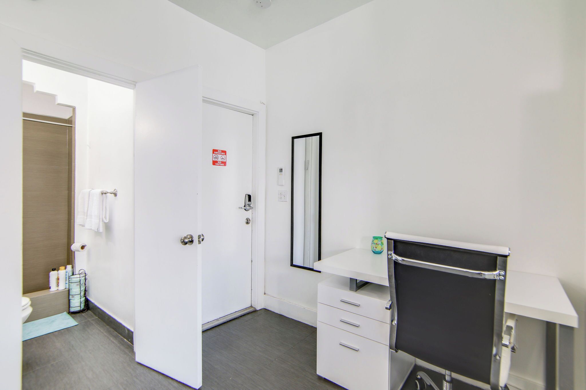 A modern bathroom with a white door, a mirror, a vanity with a black countertop, and a towel rack.