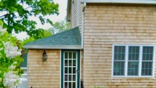Une maison à deux étages avec une façade en briques, une porte verte et un petit porche à l’avant.