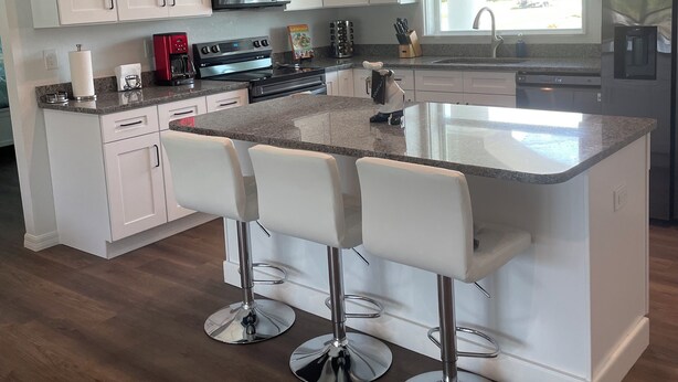 A modern kitchen with white cabinets, a central island with bar stools, stainless steel appliances, and a window providing natural light. - Fun in the Sun!
Brand New Home! (Port Charlotte)