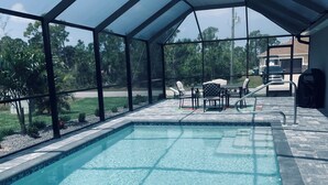 A covered outdoor swimming pool with clear water, surrounded by a patio area with chairs and a table. - Fun in the Sun!
Brand New Home! (Port Charlotte)