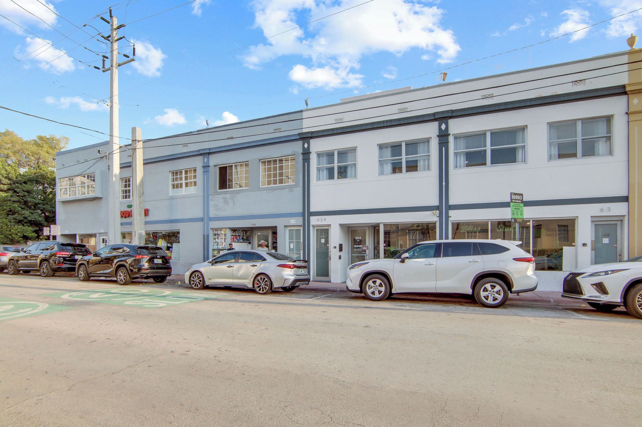 A street view with a row of parked cars, a building with multiple windows, and a visible sign.