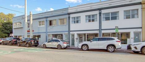 A street view with a row of parked cars, a building with multiple windows, and a visible sign.
