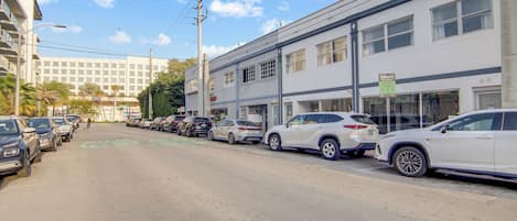 Une rue bordée de voitures garées et un immeuble doté de nombreuses fenêtres et d’une enseigne.