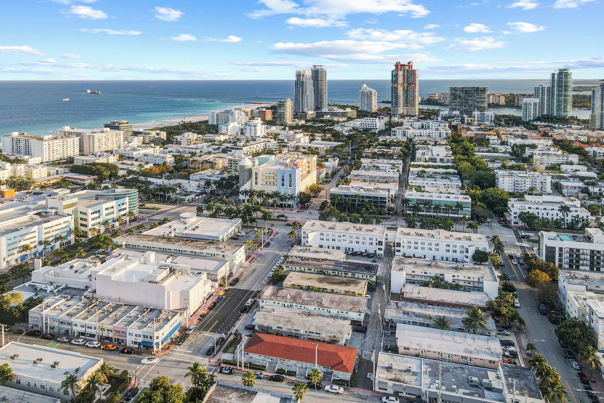 An aerial view of a coastal city with a mix of high-rise and low-rise buildings, a clear blue sky, and the ocean in the background.