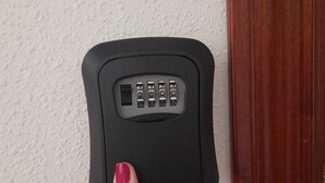 Een hand houdt een zwart apparaat met keypad vast voor een structuurwand.