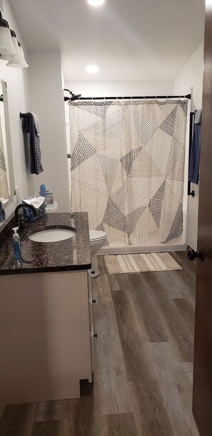 A modern bathroom with a patterned shower curtain, a sink with a marble countertop, and a toilet. - Serene Riverside Retreat by RedAwning (Little Suamico)