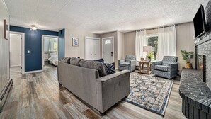 Ein Wohnzimmer mit grauem Sofa, einem gemusterten Teppich und einem Kamin.