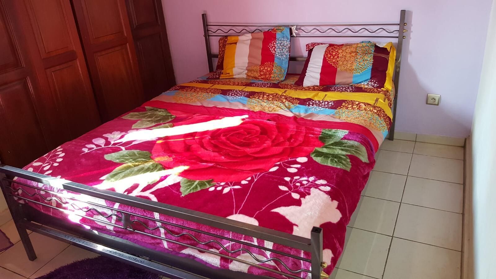 Un letto con una coperta a fiori, una struttura in metallo e una porta in legno sullo sfondo.