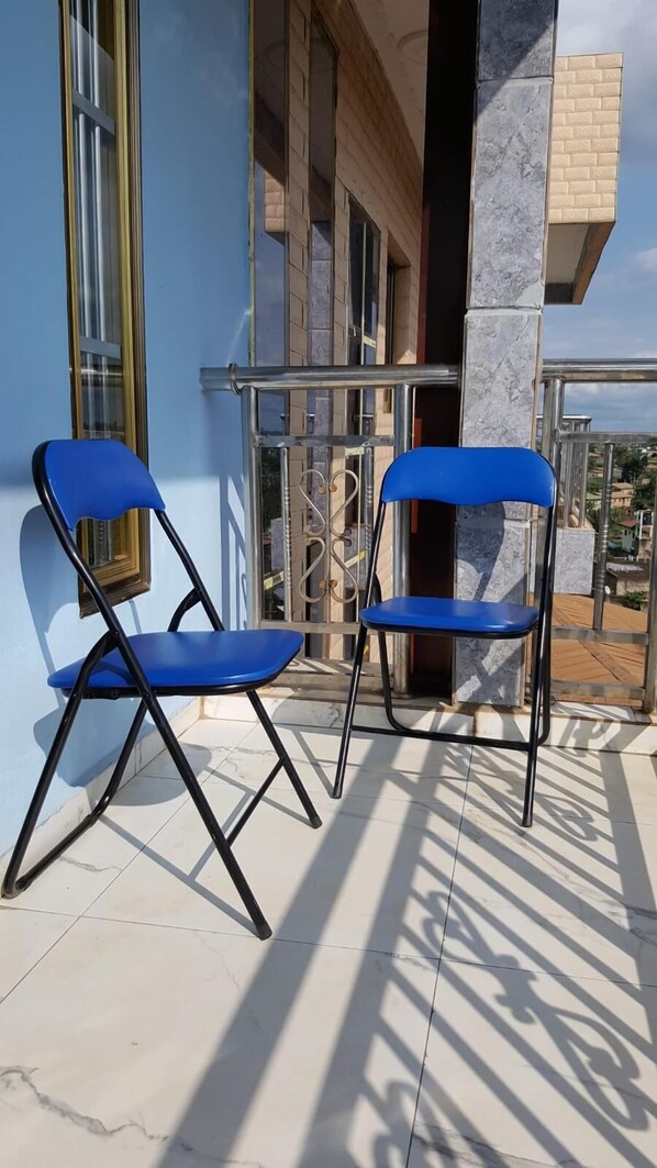 Deux chaises pliantes bleues sont posées sur une terrasse carrelée, avec un bâtiment visible à l’arrière-plan.
