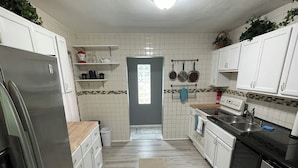 A kitchen with white cabinets, a stainless steel refrigerator, a black dishwasher, and a tiled backsplash. - Florida Beach Cottage 3BR-2BA + Den (Nokomis)