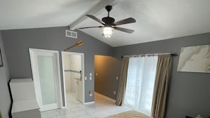 A bedroom with a bed, a ceiling fan, and a bathroom visible through an open door. - Florida Beach Cottage 3BR-2BA + Den (Nokomis)