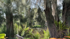 A serene outdoor seating area with wicker furniture, surrounded by lush greenery and a pond. - Florida Beach Cottage 3BR-2BA + Den (Nokomis)