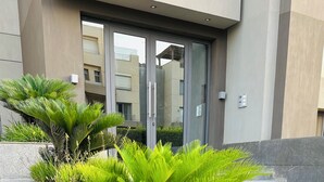 Un bâtiment moderne doté d’une entrée en verre, d’un espace paysager agrémenté d’un palmier et de fleurs, et d’un chemin en pierre.