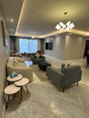 A modern living room with a sofa, armchairs, a coffee table, and a TV mounted on the wall.