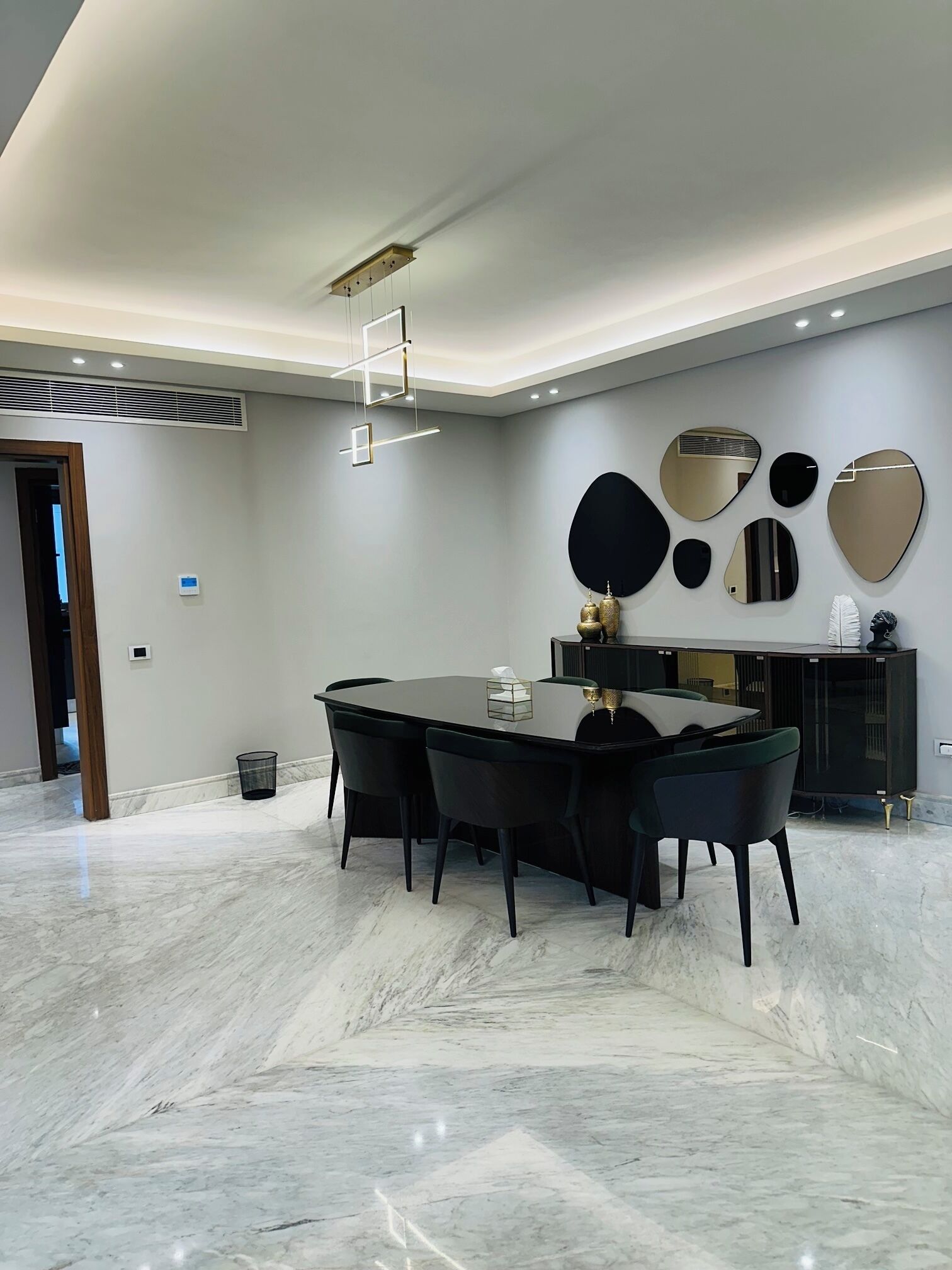 A modern dining area with a marble floor, a round table, and black chairs. There are wall-mounted mirrors and a black cabinet with decorative items.