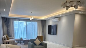 Un salon moderne avec un canapé, des fauteuils, une table basse et un téléviseur fixé au mur.