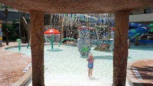 Un parque acuático con una zona central de juegos acuáticos, rodeado por un sendero de ladrillo.