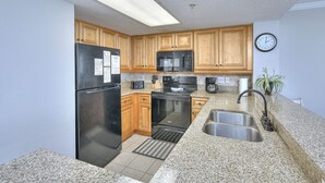 Una cocina con armarios de madera, un refrigerador negro, un microondas, un horno, un fregadero y un reloj en la pared.