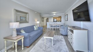 Una sala de estar con sofá, mesa de centro, televisor y una cocina al fondo.