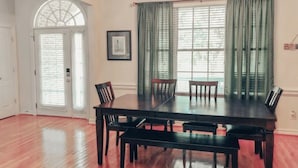 A dining room with a large table, six chairs, a chandelier, and a window with curtains.