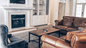 A living room with a fireplace, leather sofa, and a television on a stand.