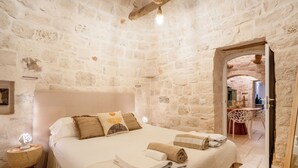 Un dormitorio con paredes de piedra, una cama, almohadas, una mesita de noche y una toalla.