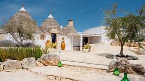 Un edificio de piedra tradicional con techos cónicos, fachada blanca y un área de entrada pavimentada con jarrones decorativos.