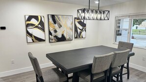 A dining area with a rectangular table and four upholstered chairs. There are three abstract paintings on the wall above the table. - 4-Bed Bungalow close to Disney, Universal Studios and many fantastic restaurants (Orlando)