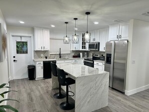 A modern kitchen with white cabinets, a marble island, stainless steel appliances, and black bar stools. - 4-Bed Bungalow close to Disney, Universal Studios and many fantastic restaurants (Orlando)