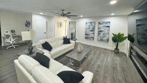 A modern living room with a white leather sofa, a coffee table, and a ceiling fan. - 4-Bed Bungalow close to Disney, Universal Studios and many fantastic restaurants (Orlando)