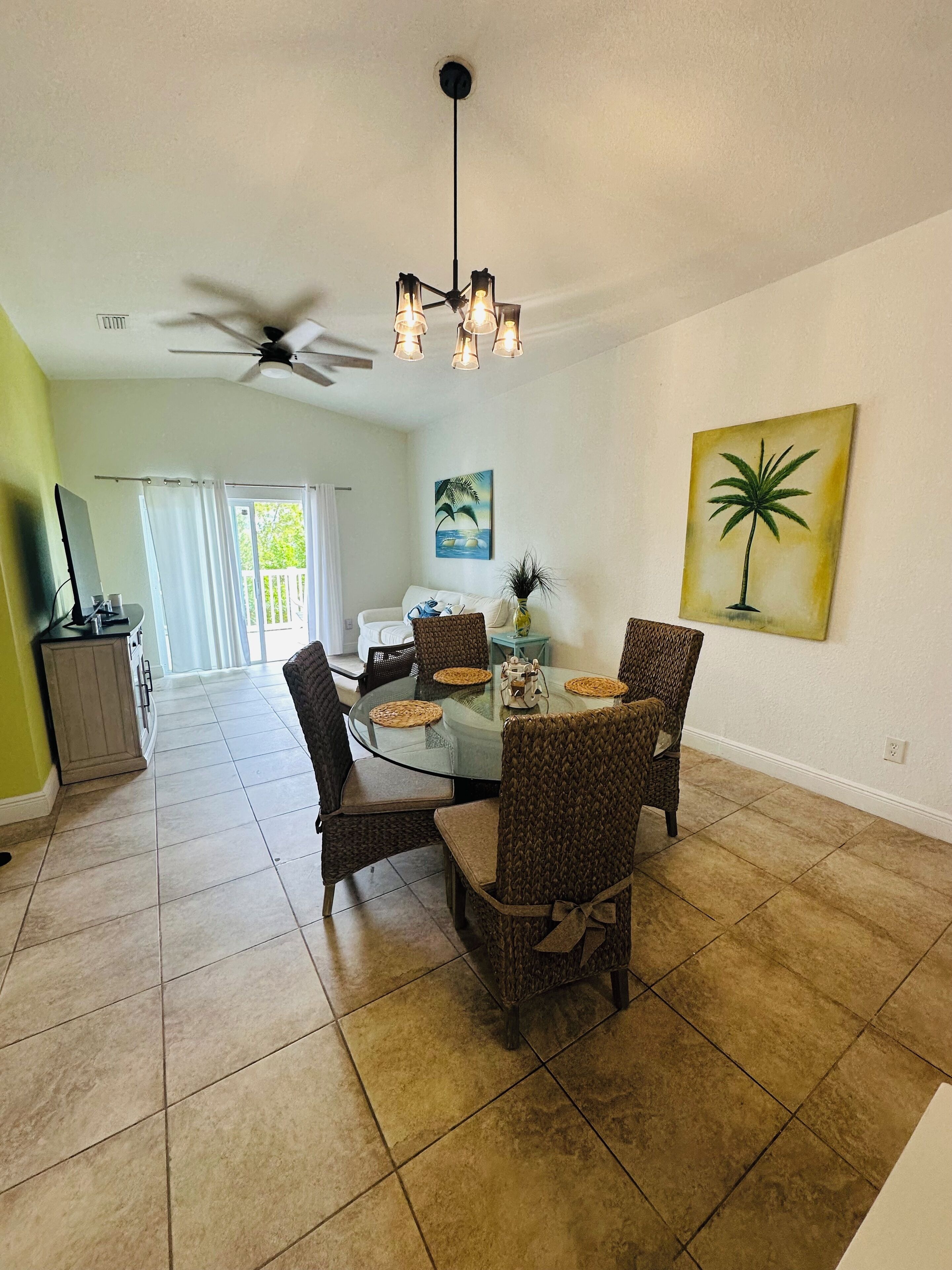 A dining area with a round glass table, wicker chairs, and a ceiling fan.