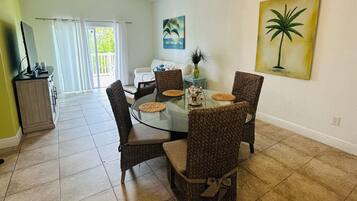A dining area with a round glass table, wicker chairs, and a ceiling fan.